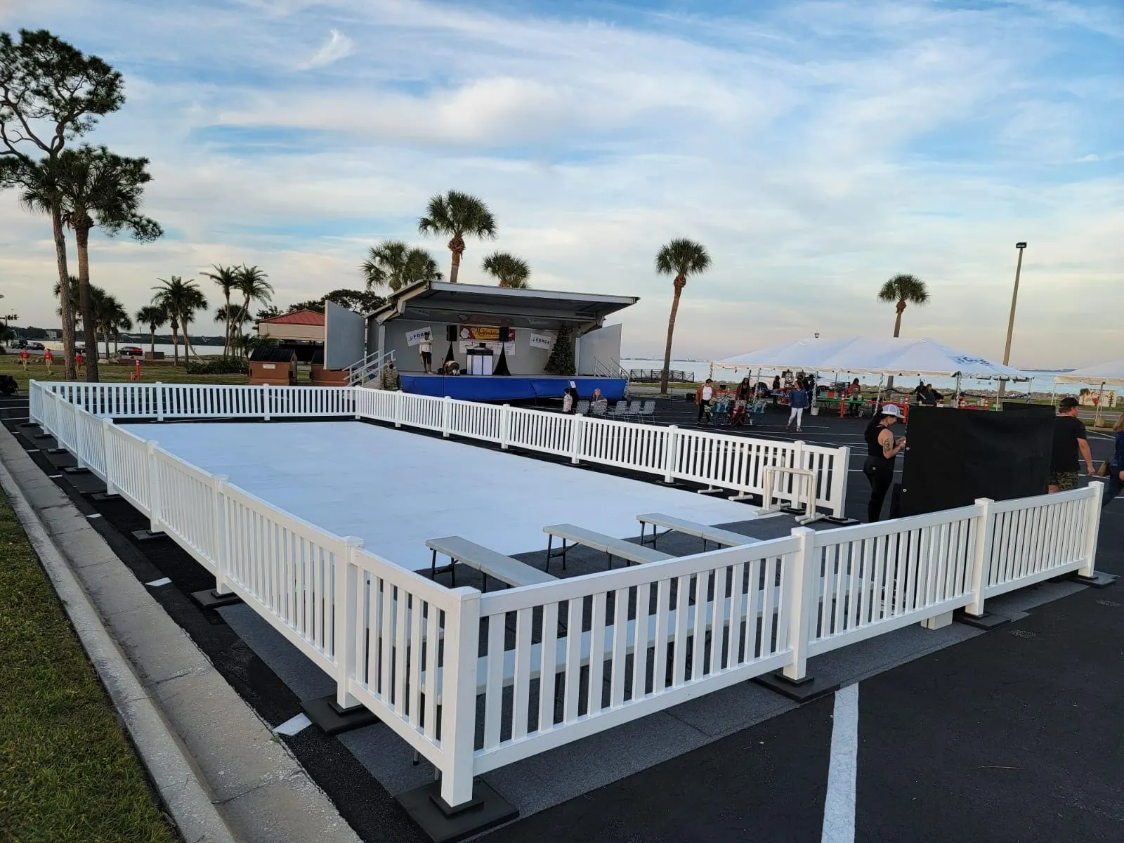 Outdoor ice rink with white fence next to palm trees, festival stage and tents. Outdoor ice rink with white fence next to palm trees, festival stage and tents.