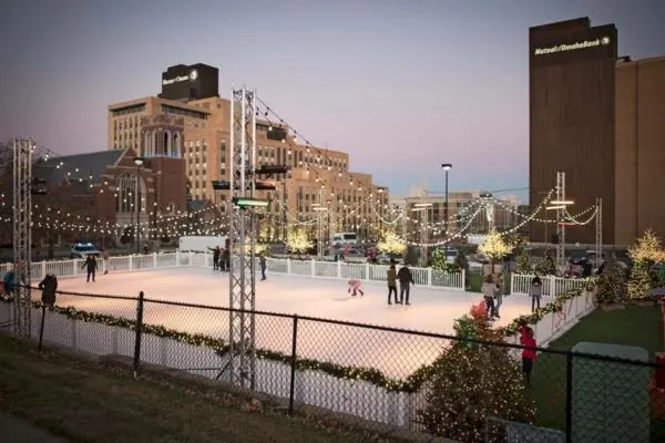 Large outdoor fenced ice skating rink in city downtown with skaters and clear draped rink lights. Large outdoor fenced ice skating rink in city downtown with skaters and clear draped rink lights.