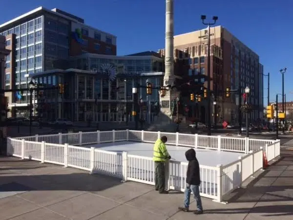 Small outdoor ice skating rink at downtown city intersection with white fence and two people. Small outdoor ice skating rink at downtown city intersection with white fence and two people.
